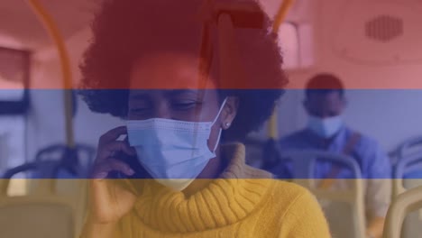 animation of flag of columbia over african american woman in face mask using smartphone in bus