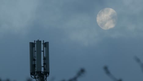 nube que pasa la luna detrás de la antena de la torre de transmisión de telecomunicaciones celulares