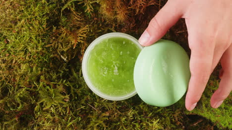 bottle of cosmetics cream serum on moss forest background green leaves. woman make up healthy natural products.