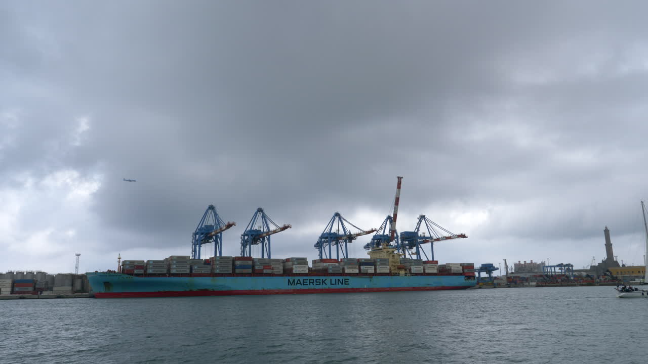 Maersk cargo ship container unloading in Genoa harbor, cloudy day. Static.