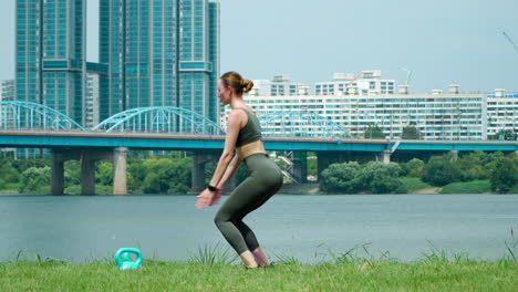 fit fitness woman performing two legs squat jump exercises working out at han river seoul city park on summer day