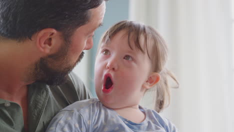 Nahaufnahme-Eines-Vaters-Mit-Down-Syndrom-Tochter,-Der-Zu-Hause-Gemeinsam-Ein-Buch-Liest-Und-Lacht