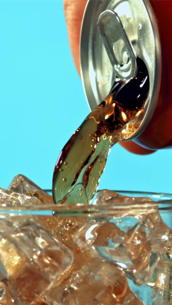 Versamento al rallentatore di cola da lattina in bicchiere con ghiaccio