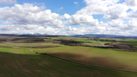 antena de campos verdes con cielo azul nublado y montañas cubiertas de nieve en la distancia