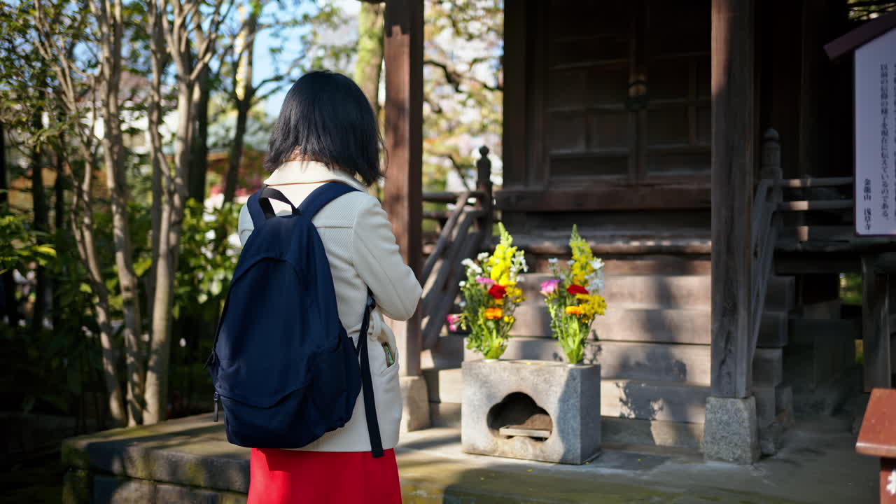 Woman praying near a wooden informational sign with a blurred background at the Senso-ji temple in Asakusa, Tokyo, Japan. Translation: "Information about the Mitsumine Shrine"