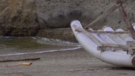 una balsa de tubos de pvc varada en una rampa de barco con olas rodando suavemente sobre la orilla rocosa, filmada de cerca