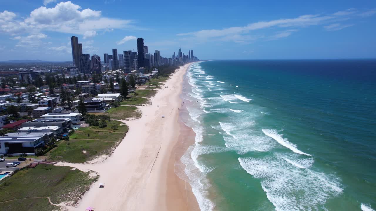 Luftfoto af sandet kystlinje langs Mermaid Beach med Gold Coast skyline i det fjerne. Et stigende træk tilbage.