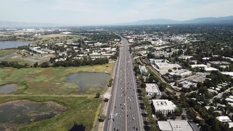 Aerial-view-of-suburbs-dense-trees-rooftop-houses-pine-trees-cars-freeway-101-marsh-on-left-hold-hover-move-forward-time-lapse