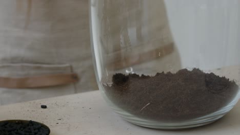 a young female botanist creates a tiny live forest ecosystem in a glass terrarium - making the first soil layer - a tight close-up