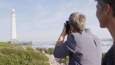 caucasian couple enjoying free time by sea on sunny day taking photo with camera