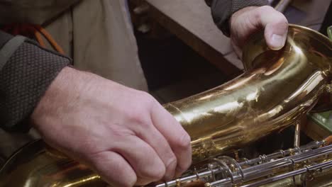 skilled instrument maker repairing big dent in golden saxophone bell by hand