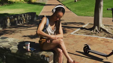 african american woman using smartwatch sitting and wearing headphones in park