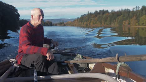 Ein-Reifer-Mann,-Der-Ruderboot-Mit-Außenbordmotor-Fährt,-Umgeben-Von-Herbstfarben