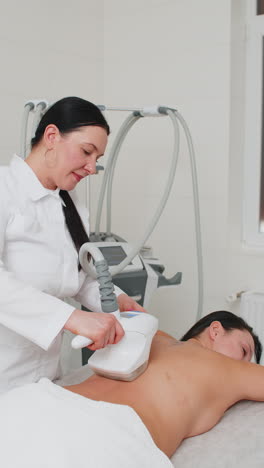 doctor makes woman cavitation lpg vacuum roller massage on back correction figures in spa clinic