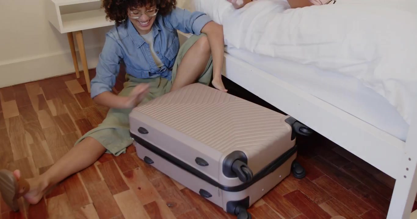 Two friends comparing passports and packing colorful clothes, closing full suitcase for travel