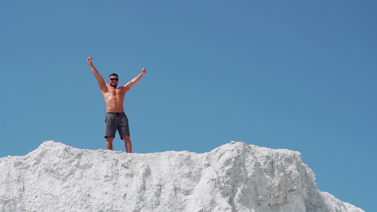 Male bodybuilder celebrates victory raising his arms high. Athlete in sunglasses on a white mountain