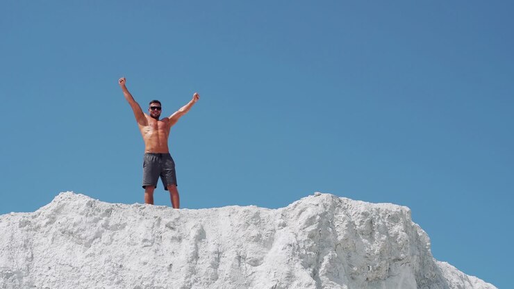 Male bodybuilder celebrates victory raising his arms high. Athlete in sunglasses on a white mountain