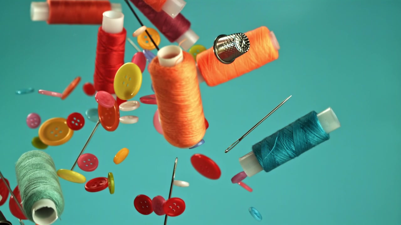 Colorful Sewing Supplies Falling in Slow Motion Against a Teal Background