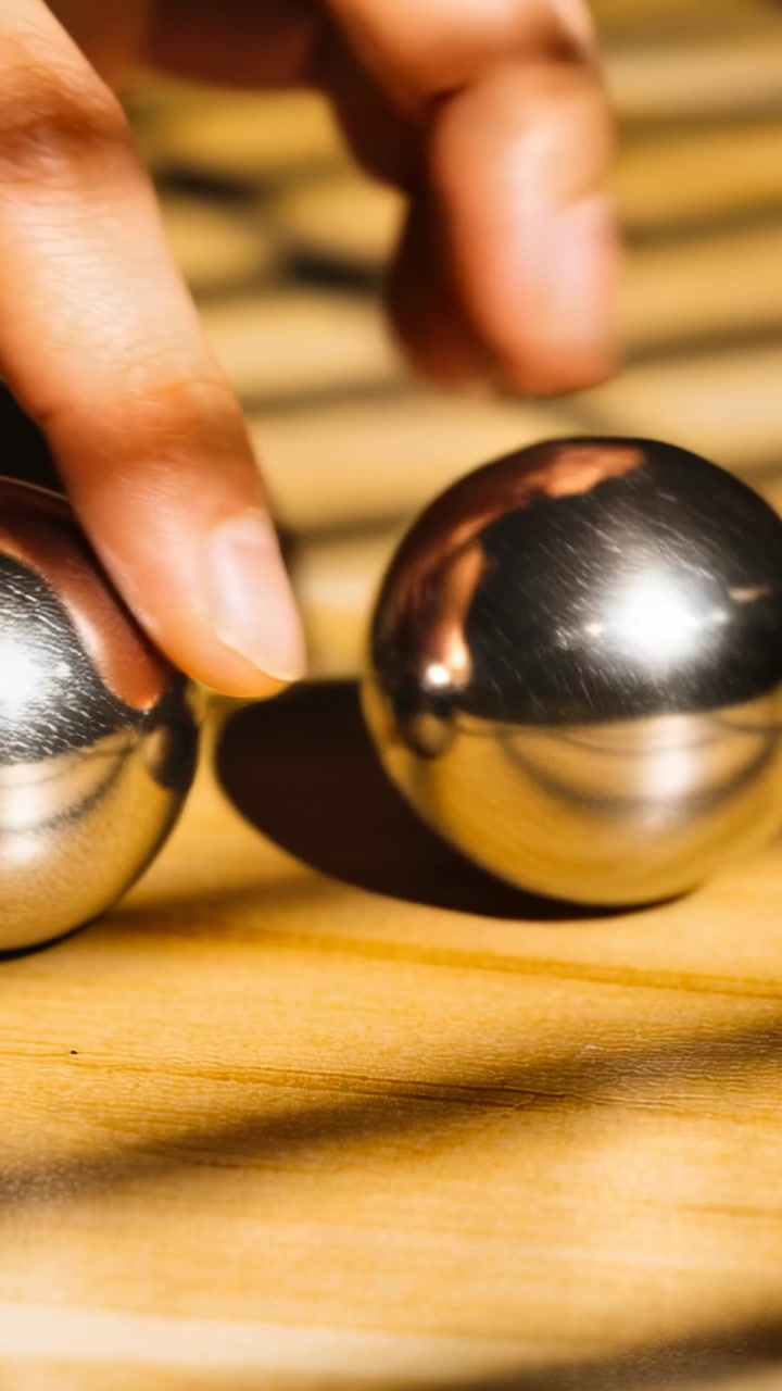 Vertical video: Hovering fingertips nudging metal spheres on wooden slats, bringing spheres closer