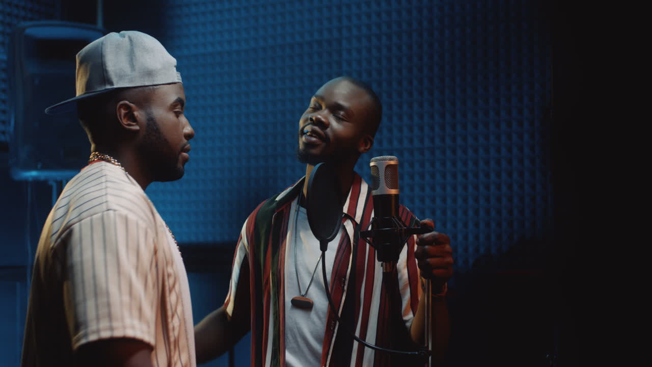 dos jóvenes cantantes guapos y elegantes grabando una canción juntos y cantando como dúo en el micrófono del estudio