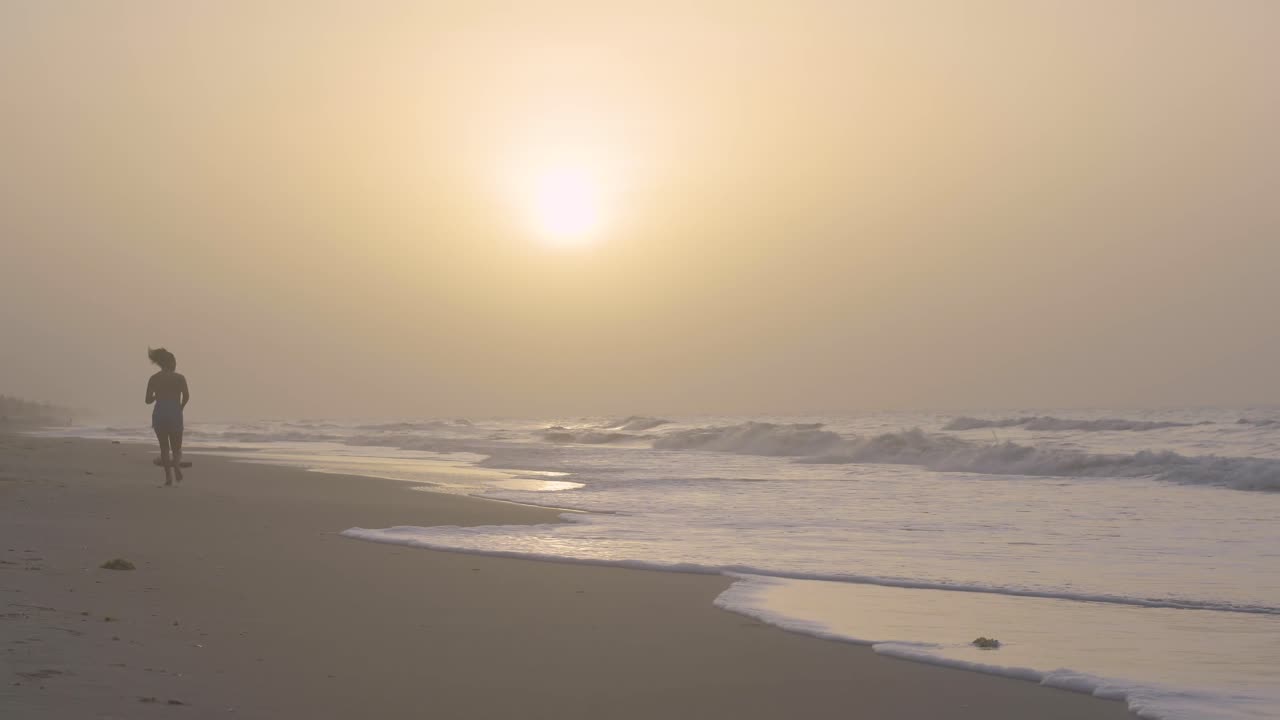 Young female runs on the sandy seashore during sunset