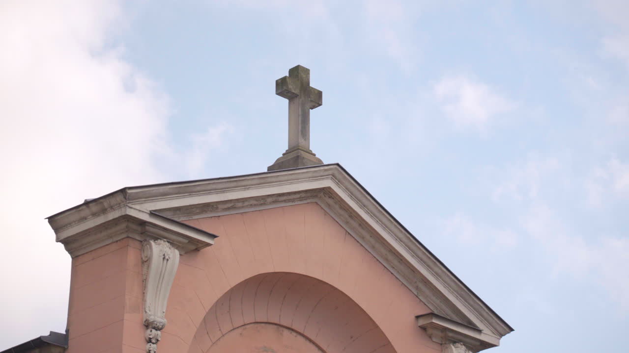 Close-up of the cross above the door of Sainte Geneviève Church in Asnières-sur-Seine. The cross is illuminated, with its silhouette visible against the cloudy sky.