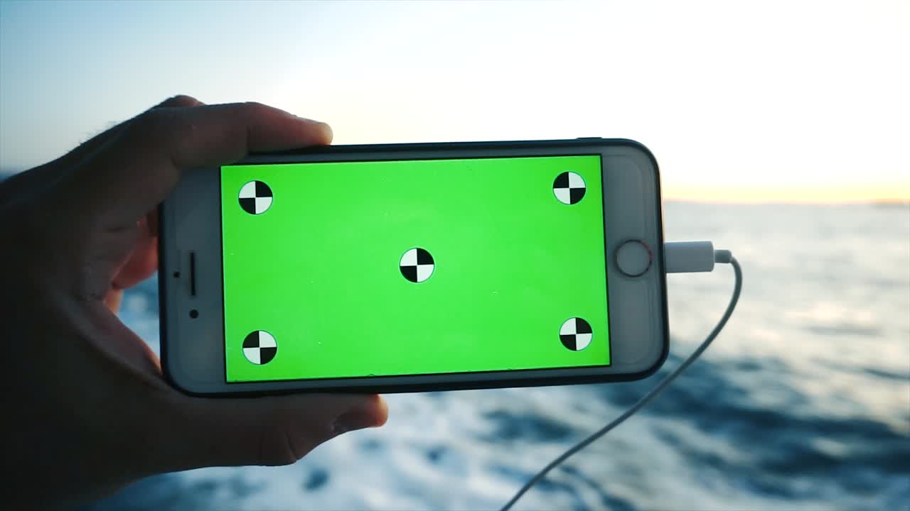 크롬 키와 함께 회전하는 스마트폰, 녹색 화면. 알파 비디오, 나무 바탕에 휴대 전화.