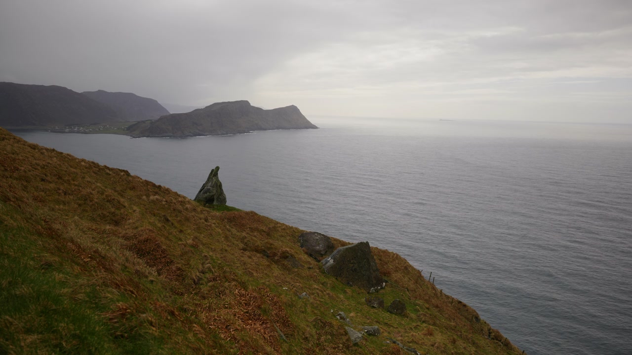 Colline marroni digradano dolcemente verso un mare calmo con una penisola in lontananza sotto un cielo nuvoloso. Adatto per video di viaggio o documentari sulla natura.