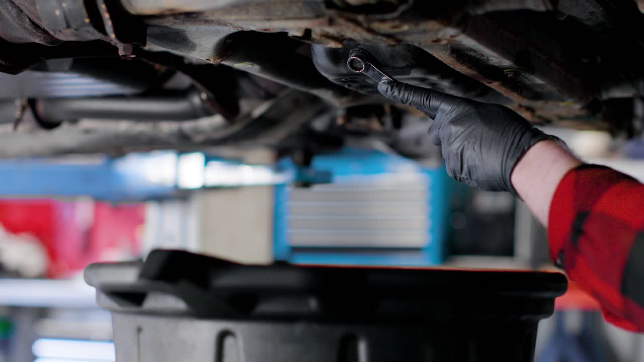 Removing drain plug and letting the oil pan empty during car maintenence. Drop the bolt in the drain pan. Static shot.