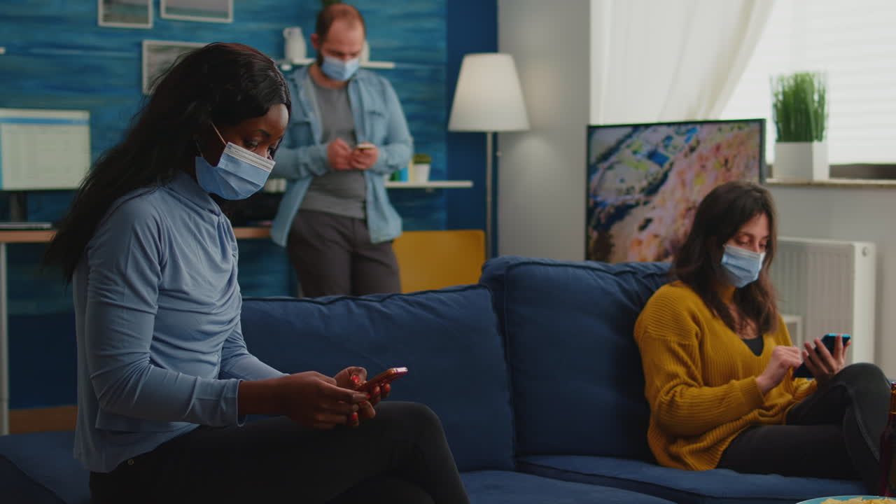 Mixed racial people sitting together in living room browsing on phones