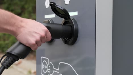 Primer-Plano-Sobre-El-Hombre-Que-Conecta-El-Coche-Eléctrico-A-La-Estación-De-Carga-Al-Aire-Libre