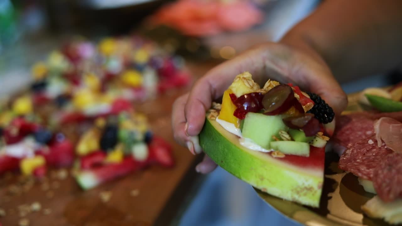 toma panorámica sobre rebanadas de sandía con una crema de yogur encima junto con granola y una variedad de frutas, como arándanos, piña, fresas y frambuesas