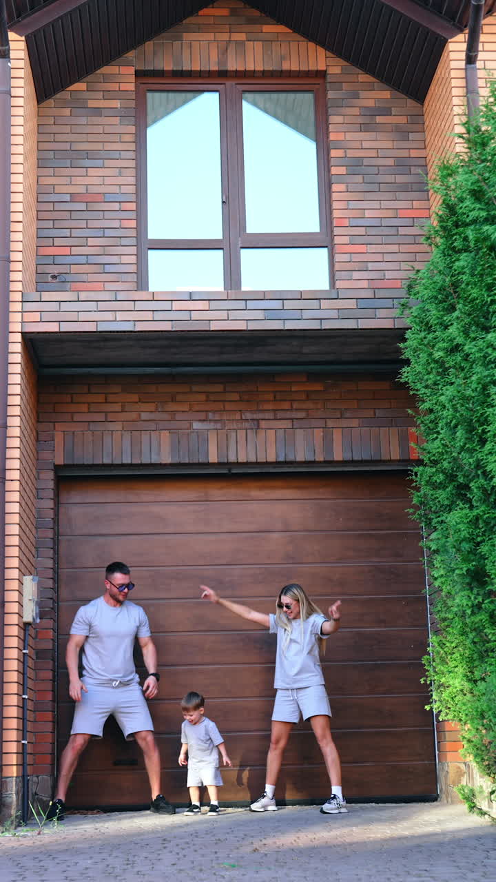 Family in matching outfits outside. A family of three stands outside their house, wearing matching grey outfits and enjoying a sunny day together