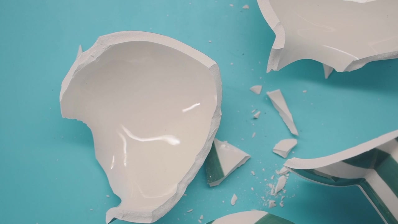 Trozos de taza de cerámica rota esparcidos sobre una superficie azul claro
