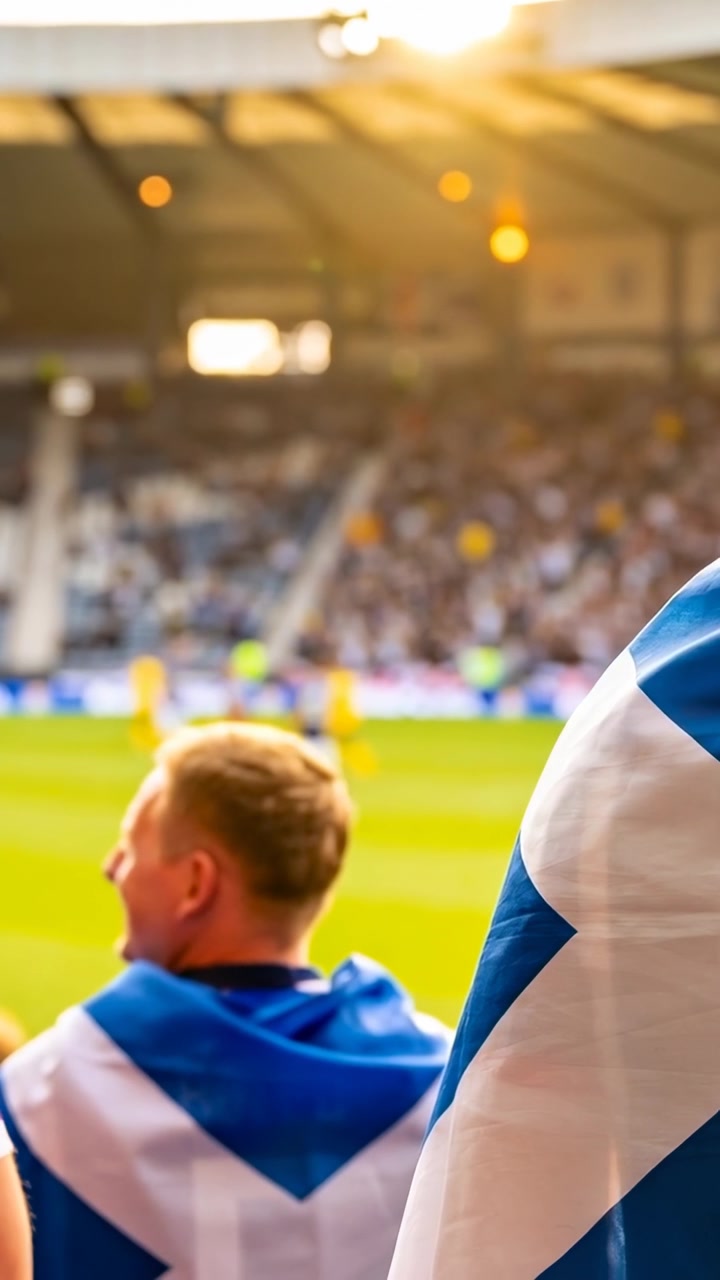 Vertikal video: Ser på kamp, supporter med blå-hvitt flagg snur hodet på stadion, solblending.