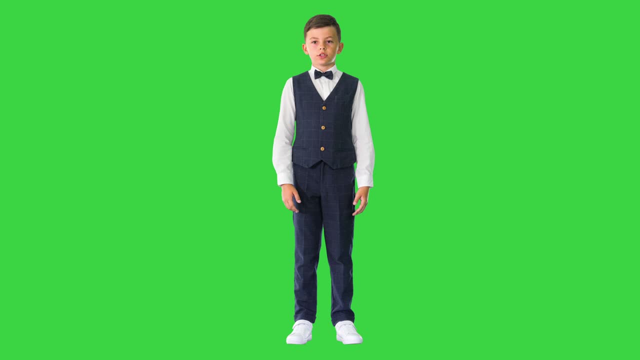 niño pequeño con corbata de papagaio y chaleco hablando con la cámara en una pantalla verde, llave de croma