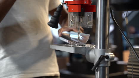 person in workshop using drill press to drill through metal rail
