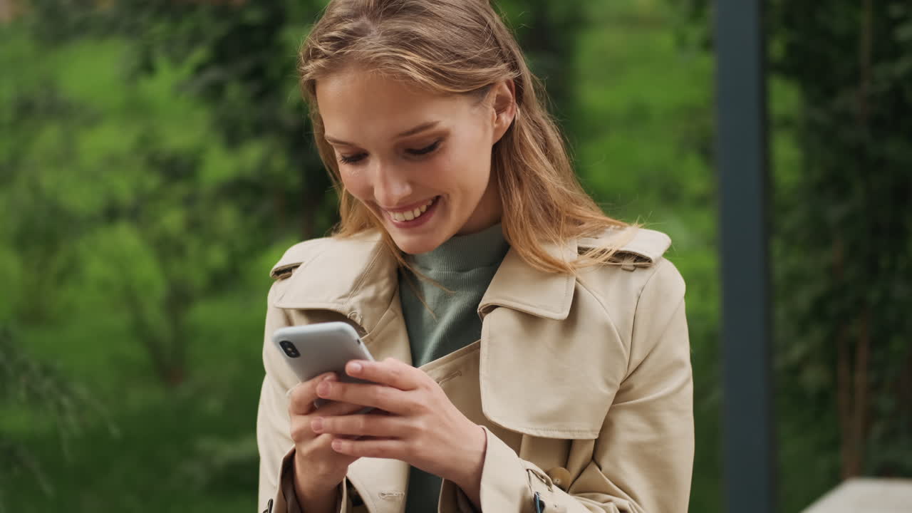 Caucasian female student using smartphone and smiling outdoors.