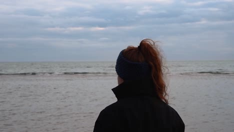 sad and melancholy beach and sea landscape with a girl with beautiful red hair watching it in a cold and windy winter day