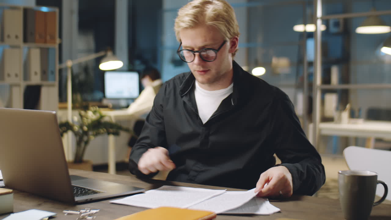 бизнесмен, подписывающий бумаги и использующий ноутбук ночью в офисе