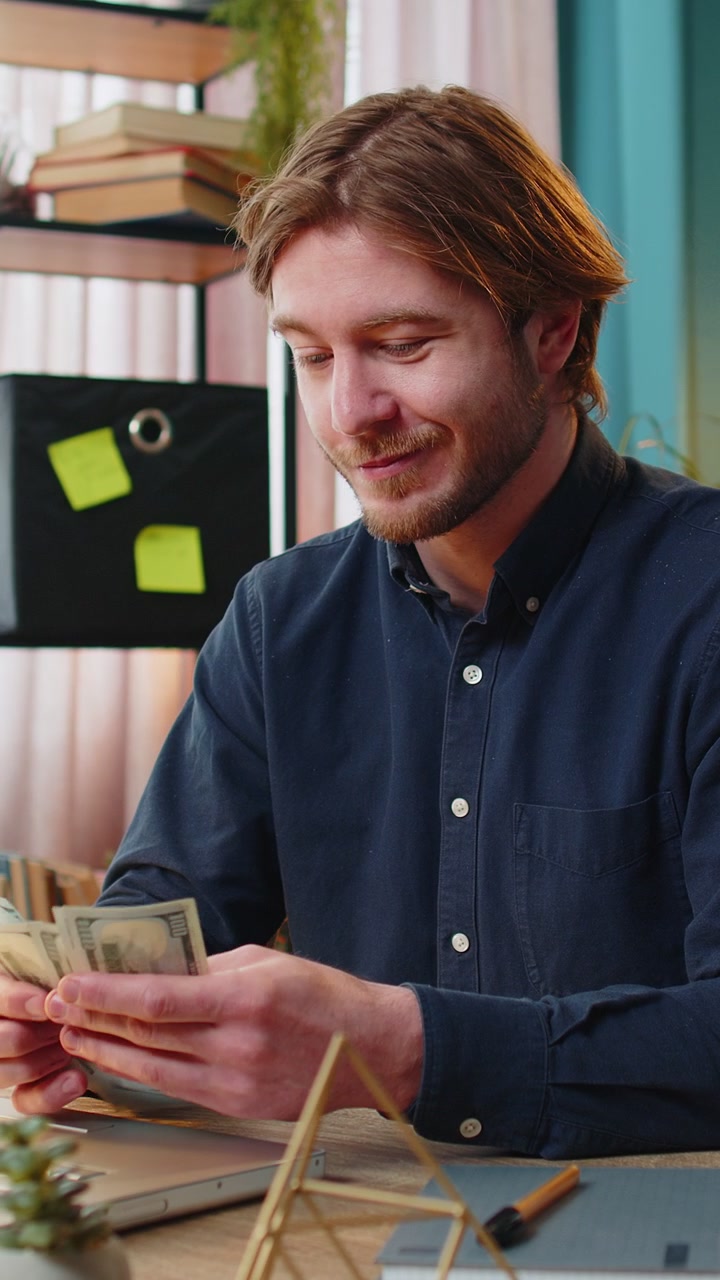 Happy rich business man counting money cash dividends salary and using laptop in home office