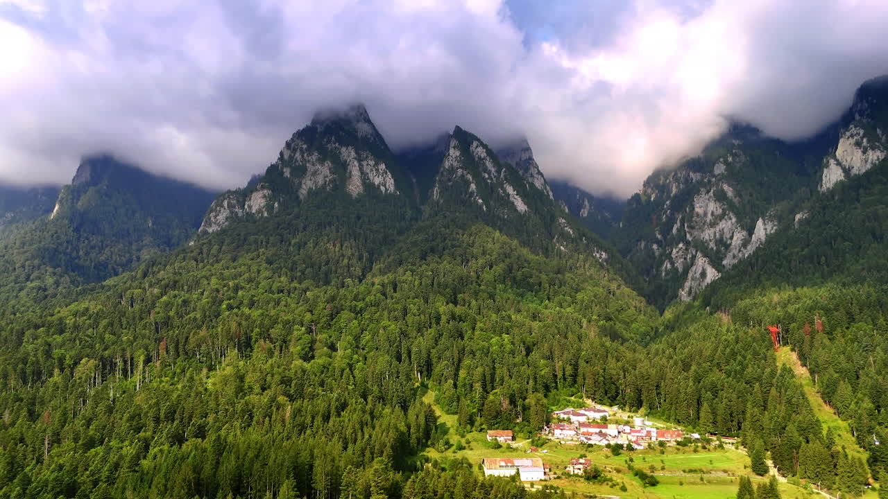 Picturesque mountain tops covered with fluffy white cloudscape. Lush evergreen pine tree woods cover the slopes of the rocks in the Bucegi Mountains, Romania