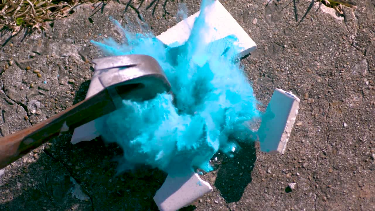 A white ceramic plate that has vivid blue chalk powder on it being smashed into pieces in slow motion with a hammer