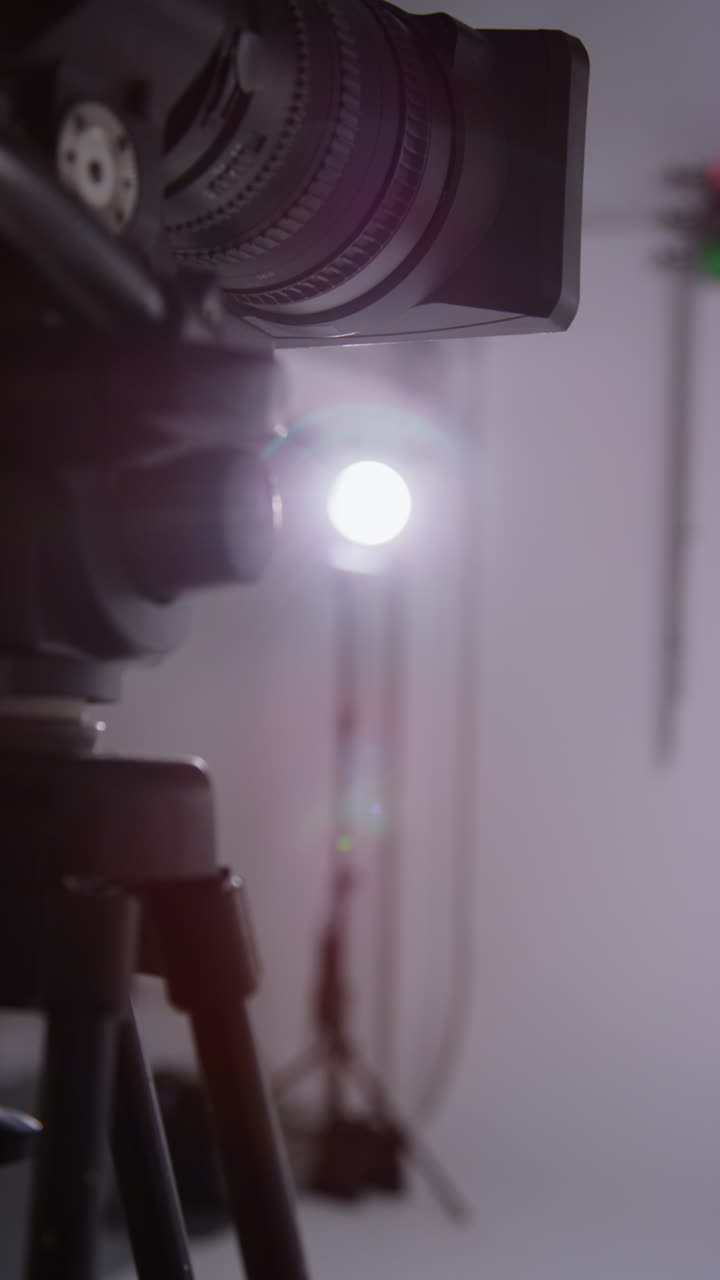 Vertical Video Close Up Of Film Or Video Camera On Tripod Shooting Movie In Studio With Light In Background
