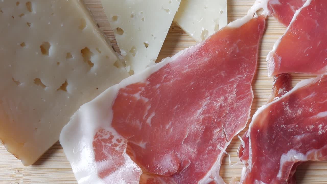 Slices of cured ham and aged cheese on a wooden board, evoking rustic dining