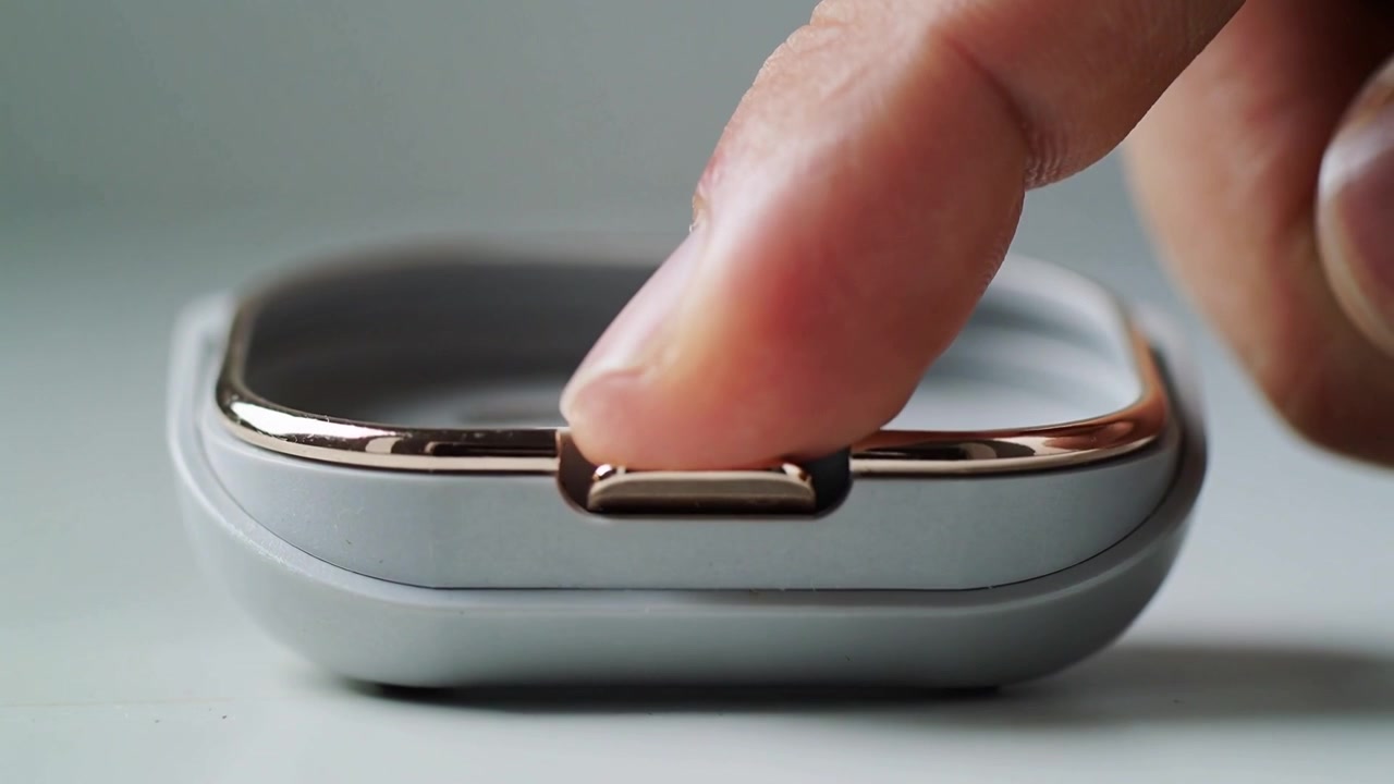 Pressing fingertip on small device popping metallic latch outward, releasing catch on tabletop