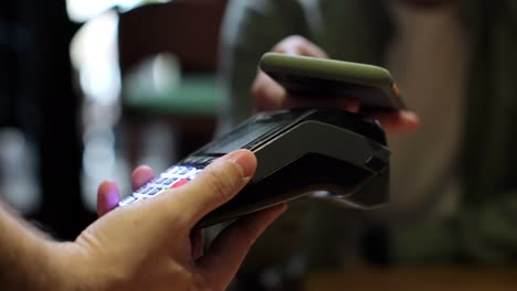 man pay by smartphone on electronic payment machine or card reader. client buys food order at coffee place.