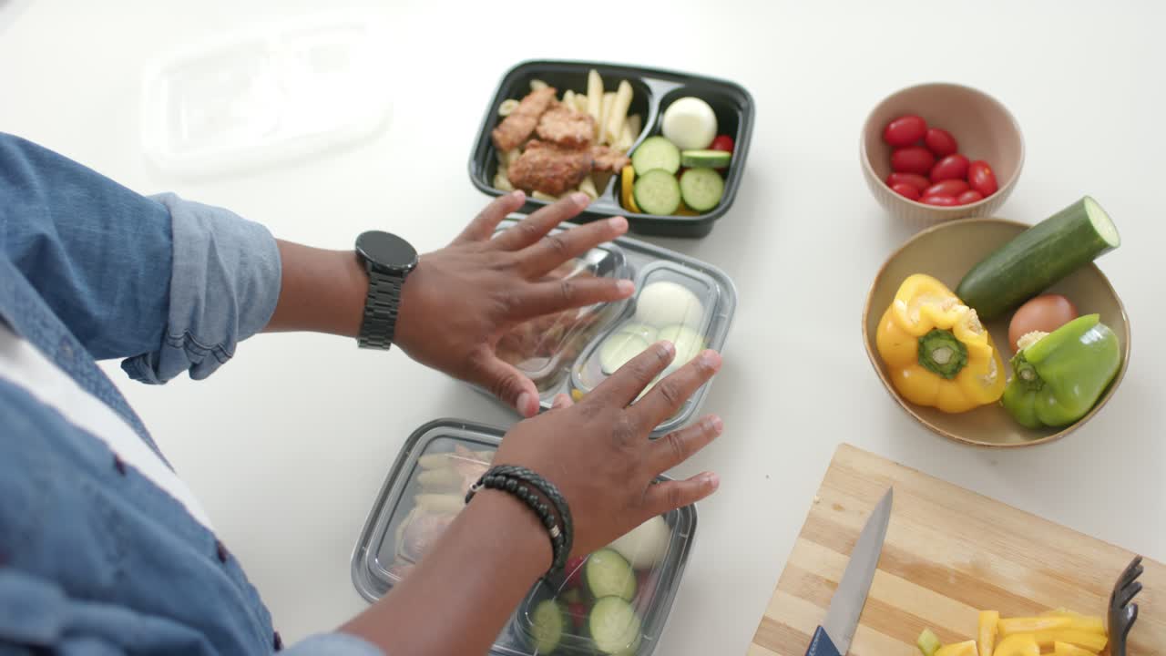 African American man reaching, placing lids on 3 trays, packing at kitchen counter, copy space