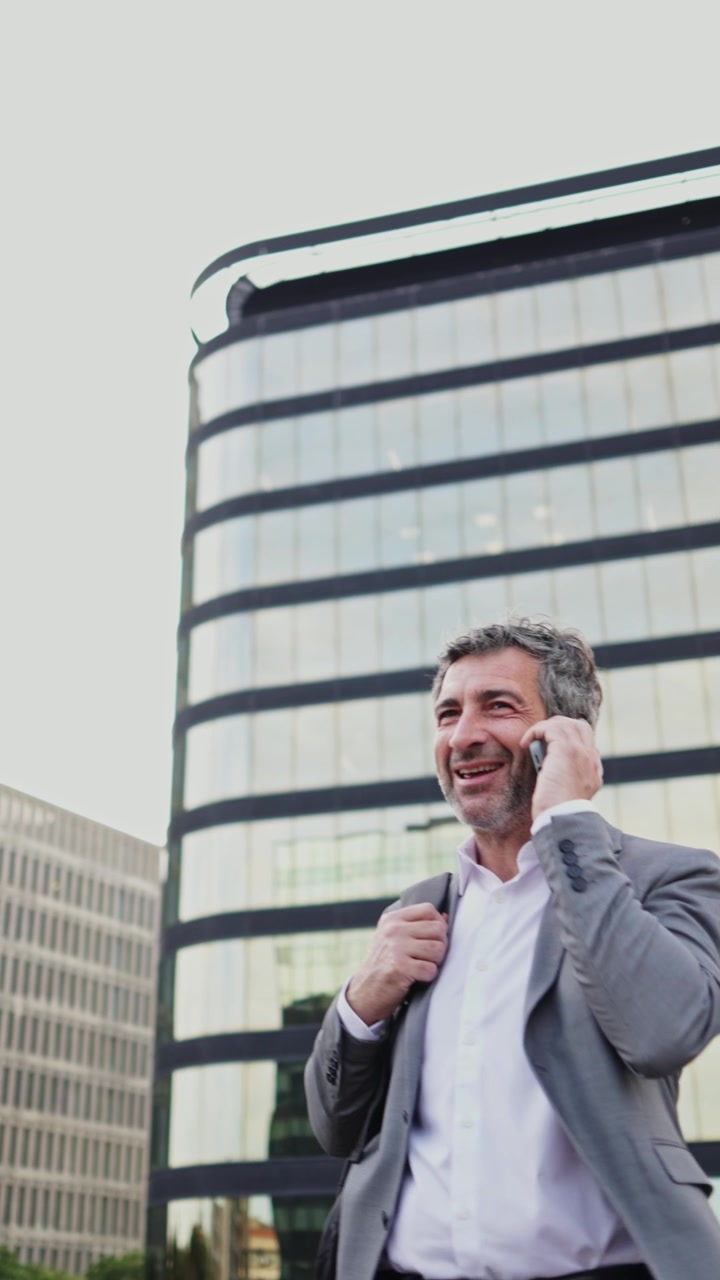 Empresario feliz hablando por smartphone frente a un moderno edificio de oficinas.