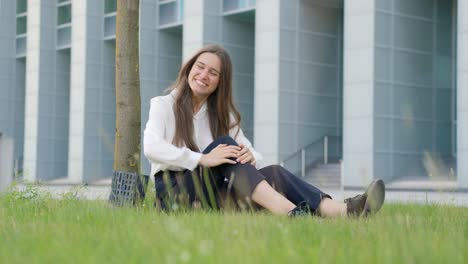 Happy-girl-sitting-on-grass-in-elegant-clothes,-spreading-arms-wide-open